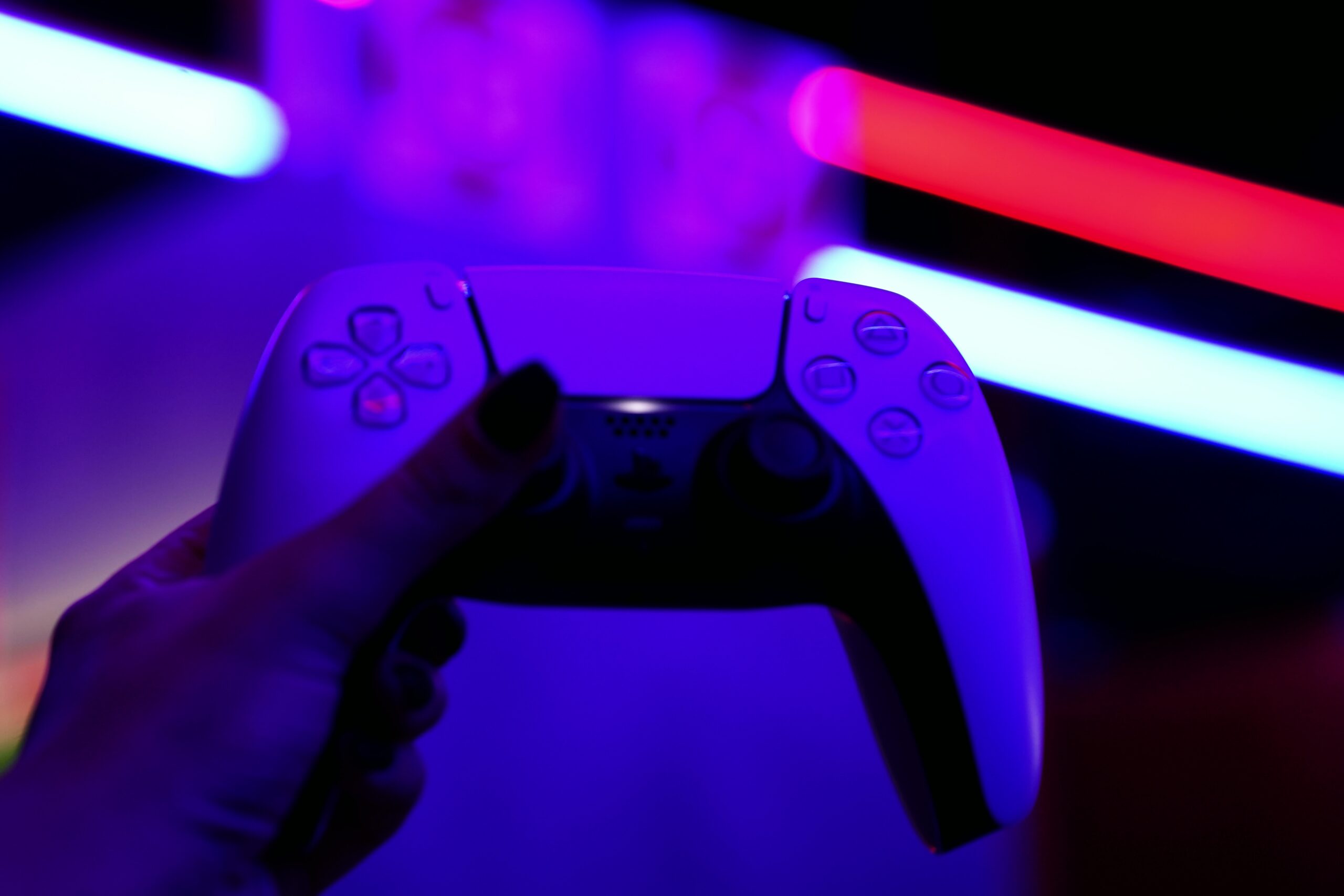 PS5 Cafe Antalya DualSense Oyun Deneyimi PS5 Cafe Antalya’da neon ışıklar altında elde tutulan DualSense kumandası